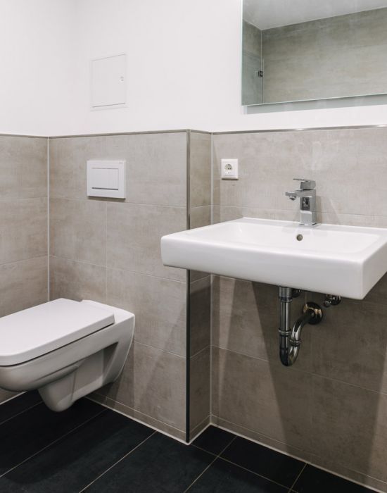 Modernes Gäste-WC mit wandhängendem WC, Waschtisch und grauen Fliesen als Referenz von F+S Haustechnik.