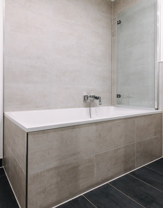 Modernes Badezimmer mit Badewanne, Glasabtrennung und grauen Fliesen als Referenz von F+S Haustechnik.
